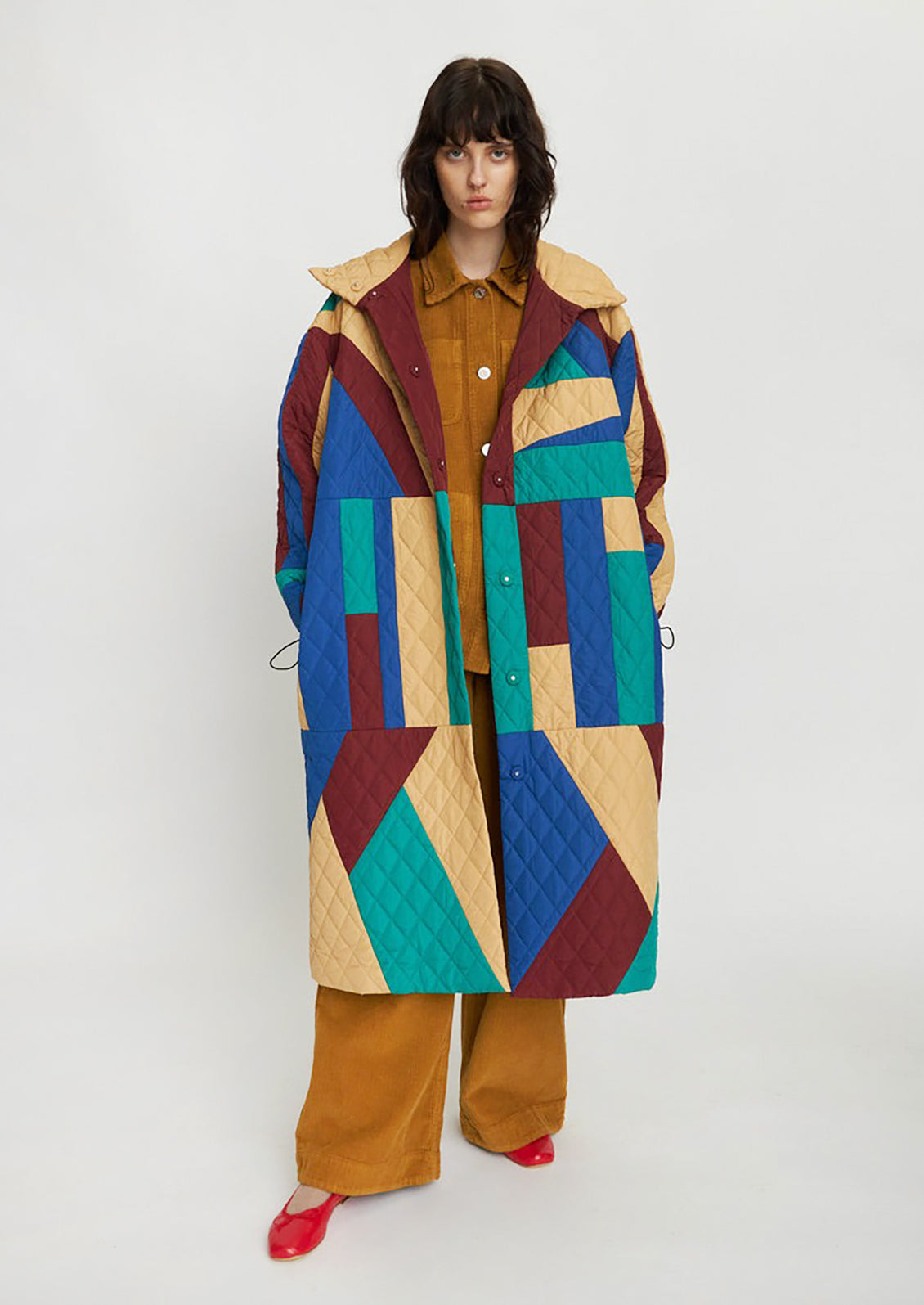 A woman wearing a geometric patchwork quilted coat in wine, teal, beige and blue.