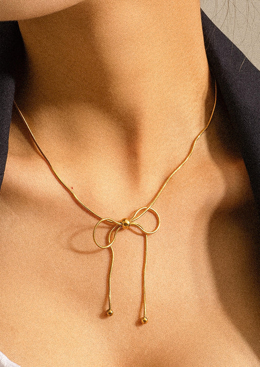 A person wearing a gold necklace made of round woven chain with bow shaped tie at front.