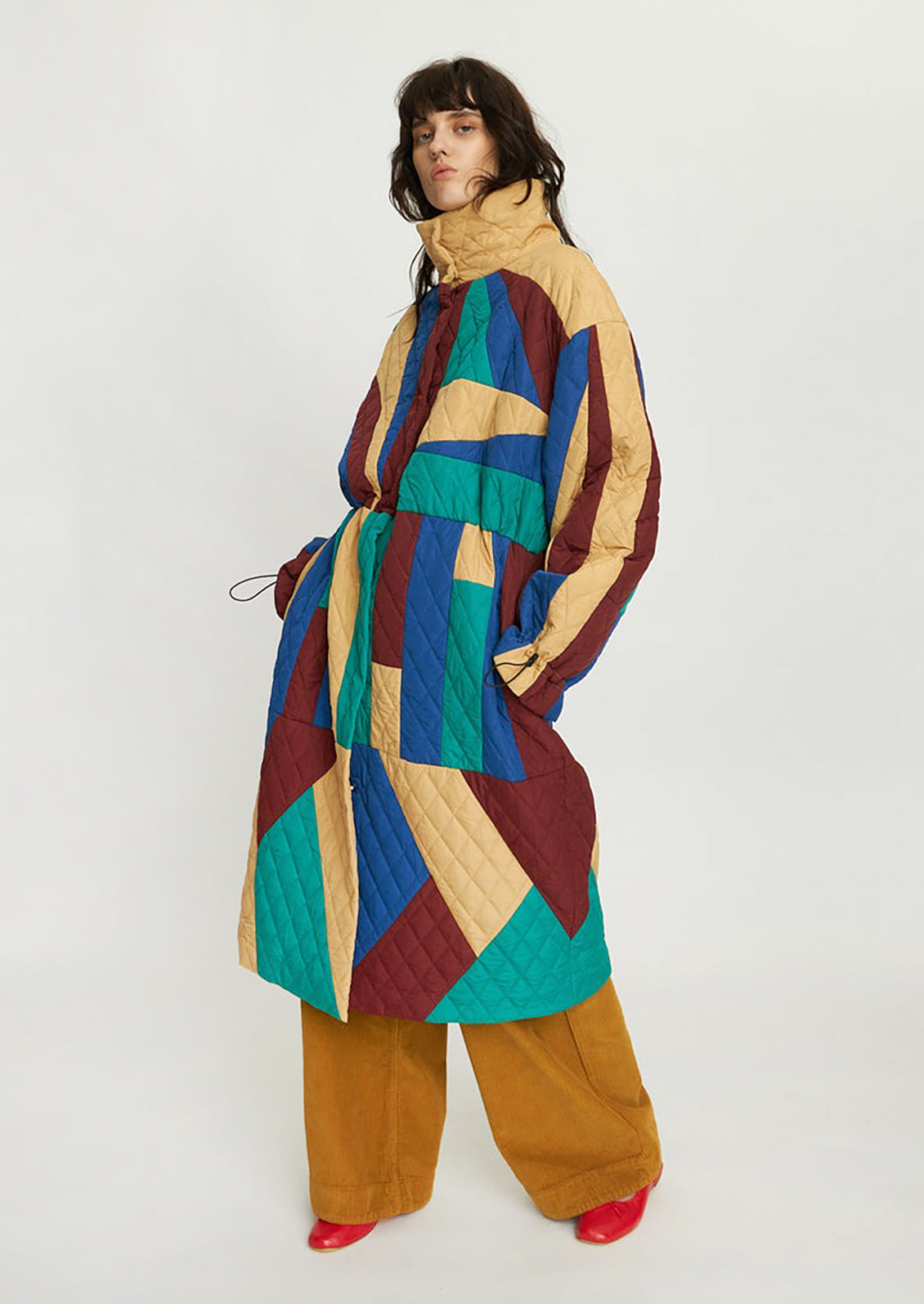 A woman wearing a geometric patchwork quilted coat in wine, teal, beige and blue.