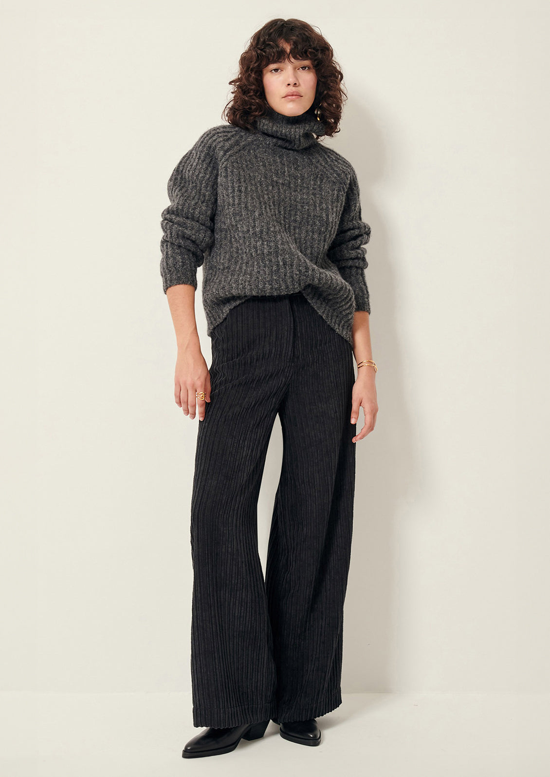 A woman wearing a pair of dark grey corduroy pants in wide leg.