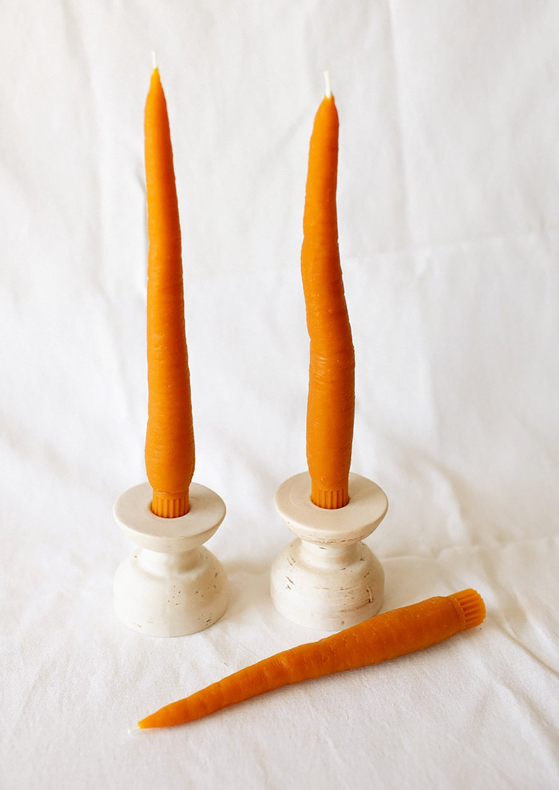 A pair of orange taper candles resembling carrots, in candle holders.