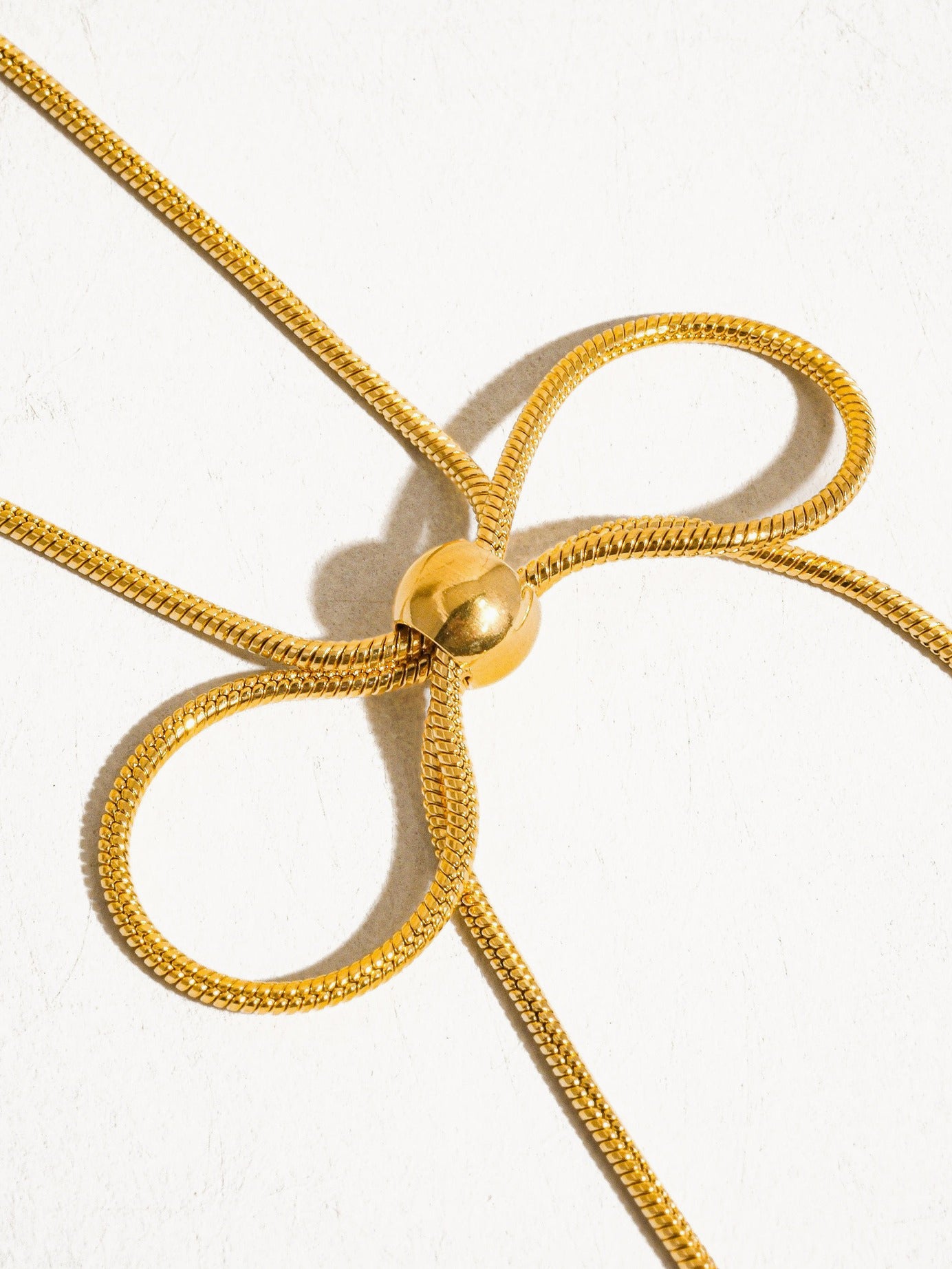 A gold necklace made of round woven chain with bow shaped tie at front.