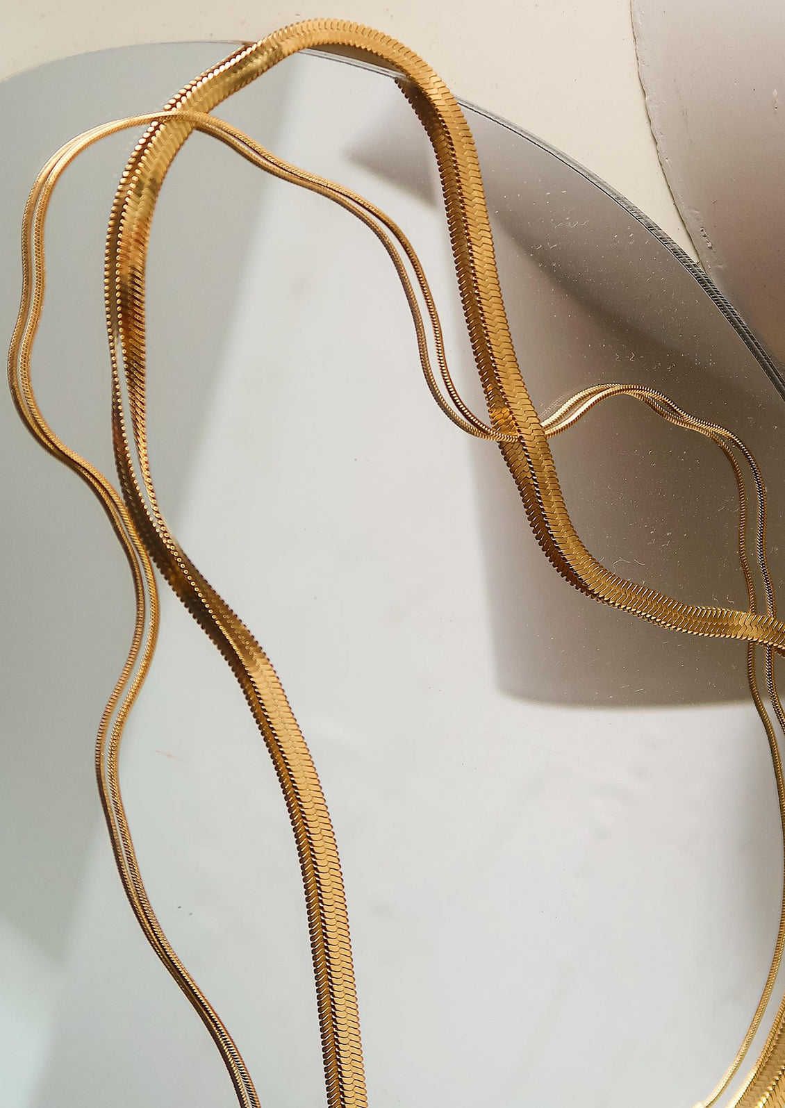 A two-in-one gold chain necklace with flat wide herringbone chain and thin round chain.