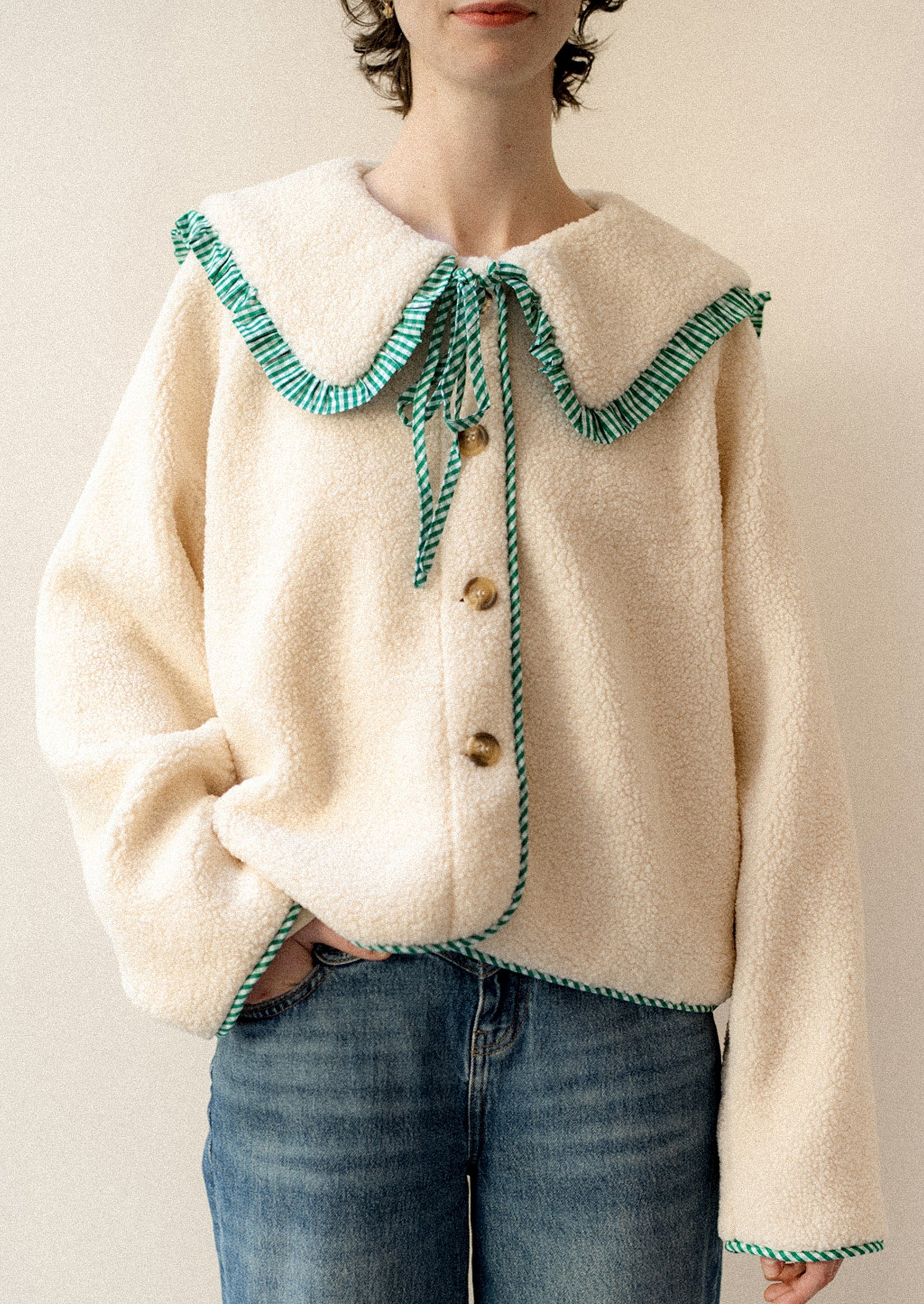 A woman wearing a cream shearling fleece jacket with green gingham trim.