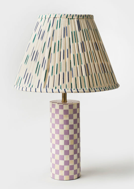 A table lamp with purple and cream checker print cylinder base with ikat printed pleated lampshade.