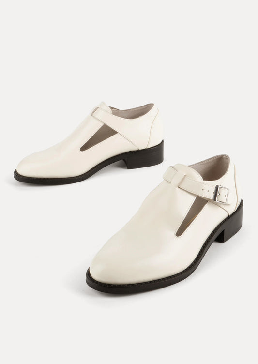 A pair of leather shoes in white with high vamp and buckle strap at ankle.