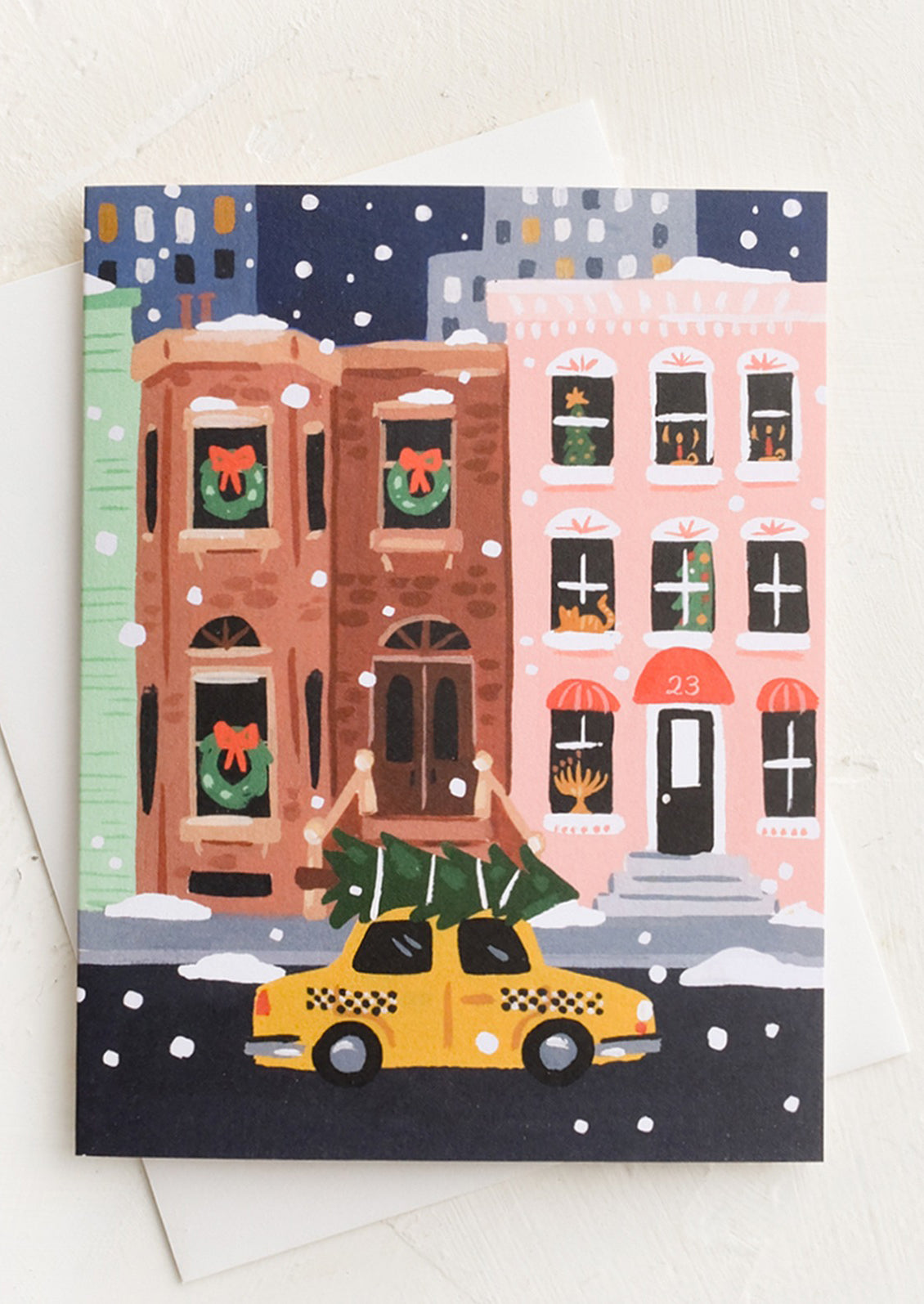 A greeting card with illustration of brownstone and taxi with Christmas tree.