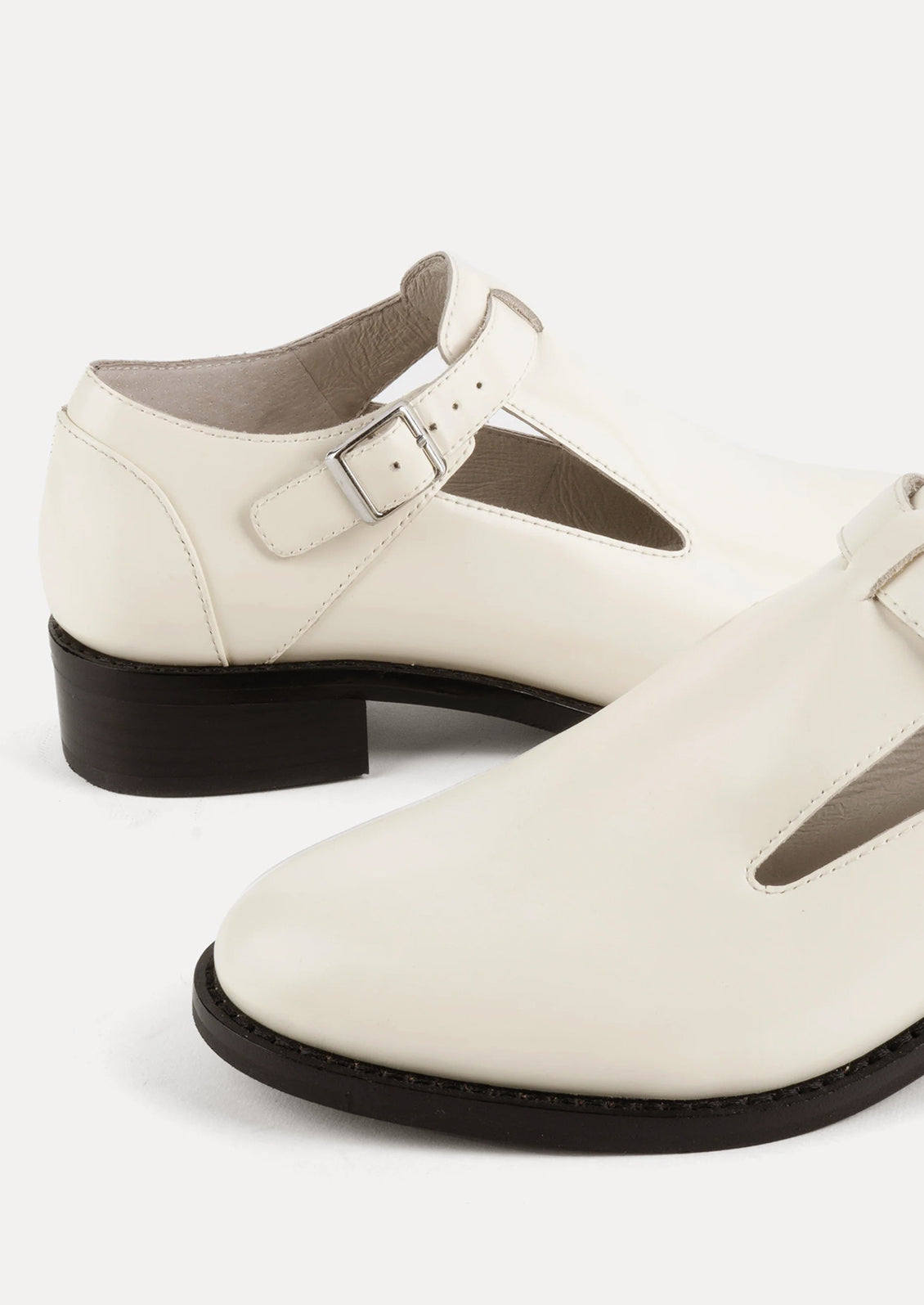 A pair of leather shoes in white with high vamp and buckle strap at ankle.