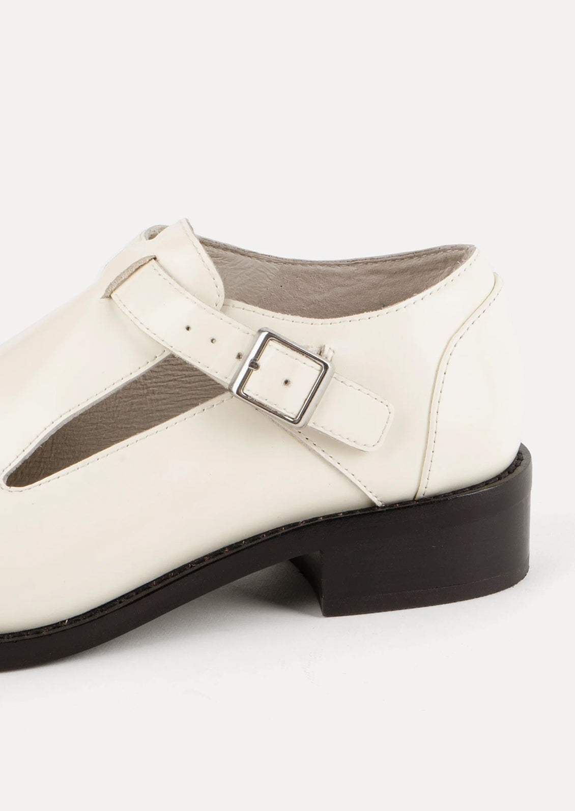 A pair of leather shoes in white with high vamp and buckle strap at ankle.