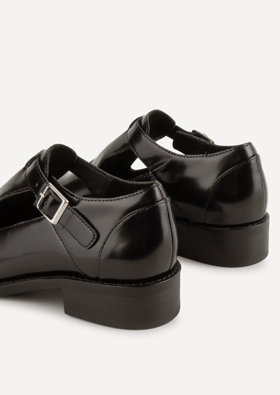 A pair of leather shoes in black with high vamp and buckle strap at ankle.