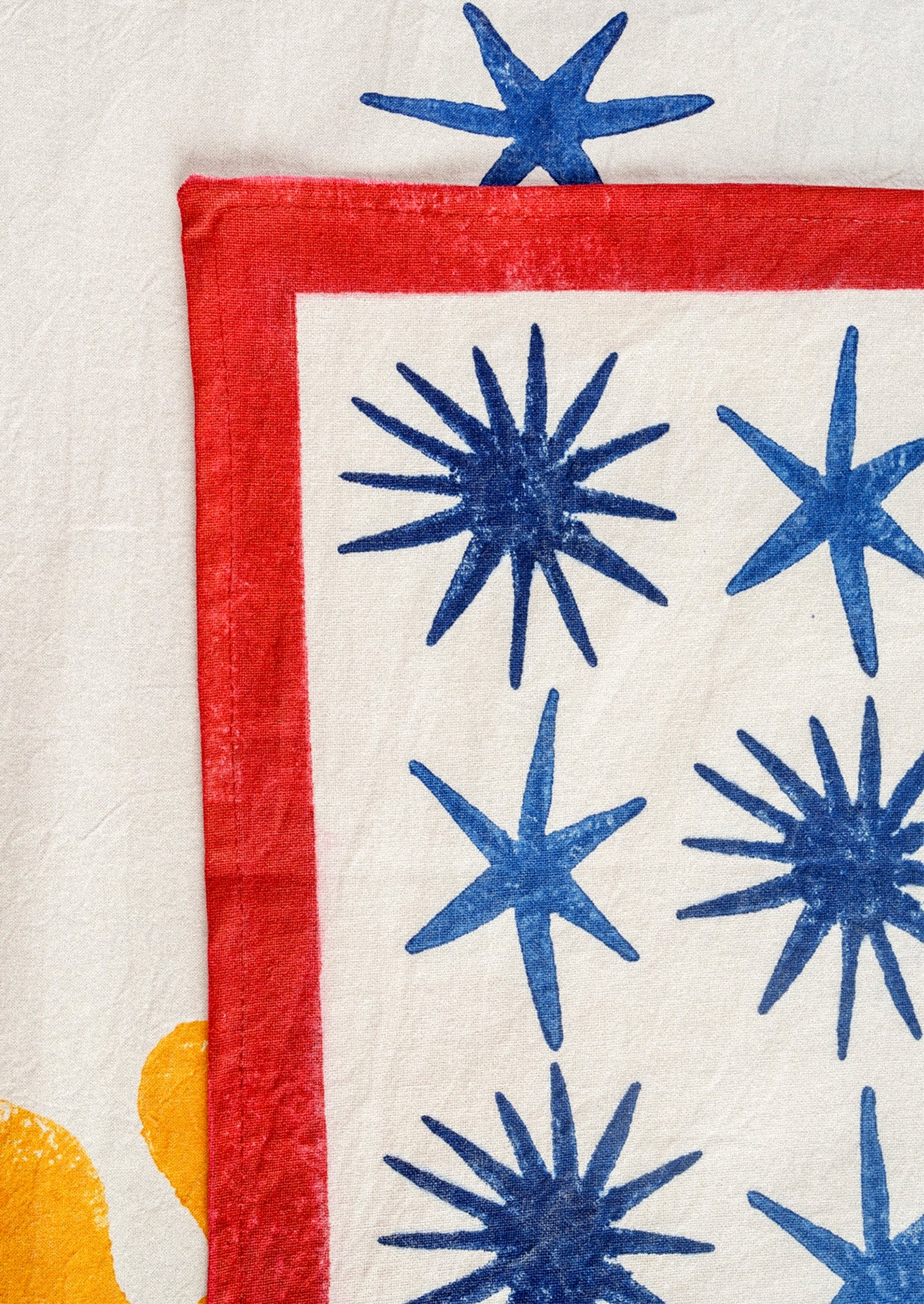 A block printed placemat in white with blue stars and red border.