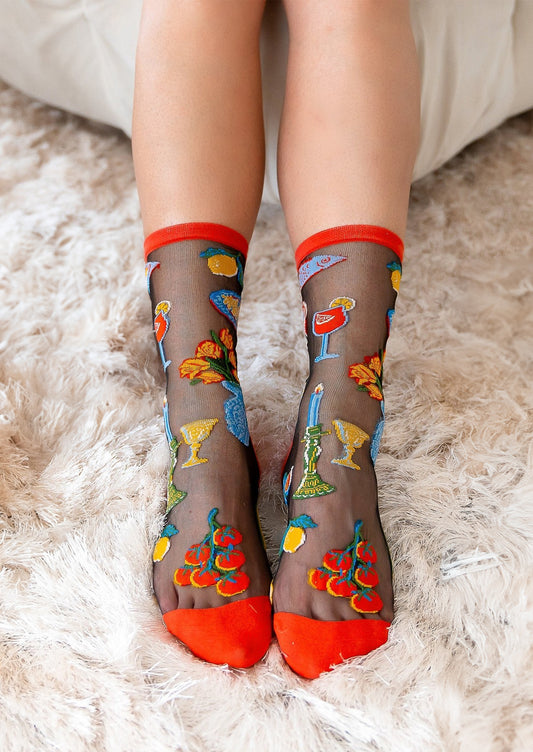 A pair of socks in sheer black with bright red trim, mixed pattern of cocktails, tomatoes, fish etc.