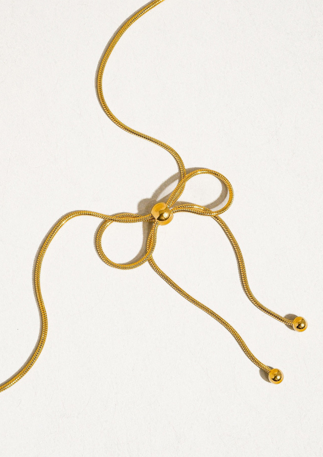 A gold necklace made of round woven chain with bow shaped tie at front.