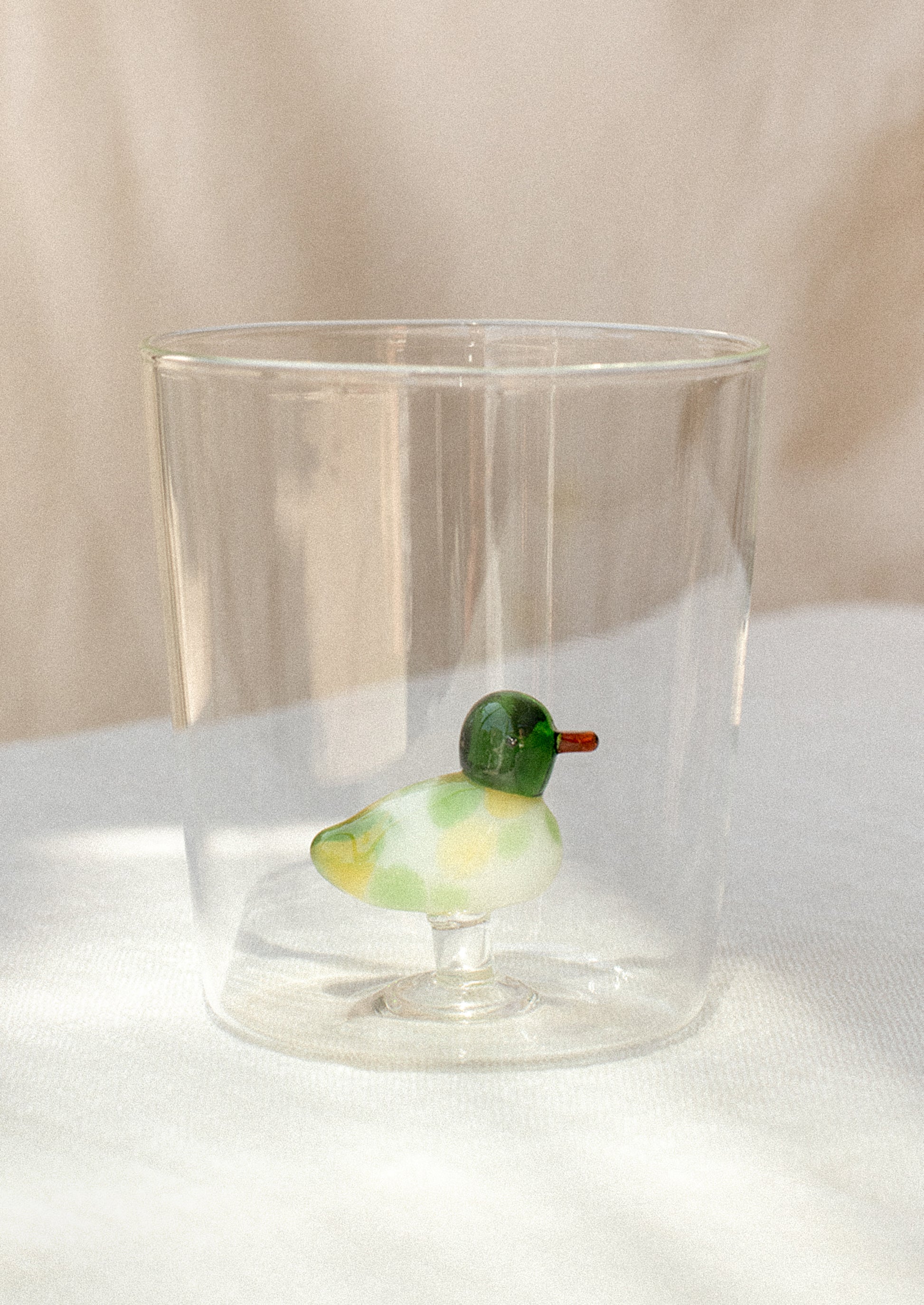 A clear glass cup with figurine of a duck at bottom.