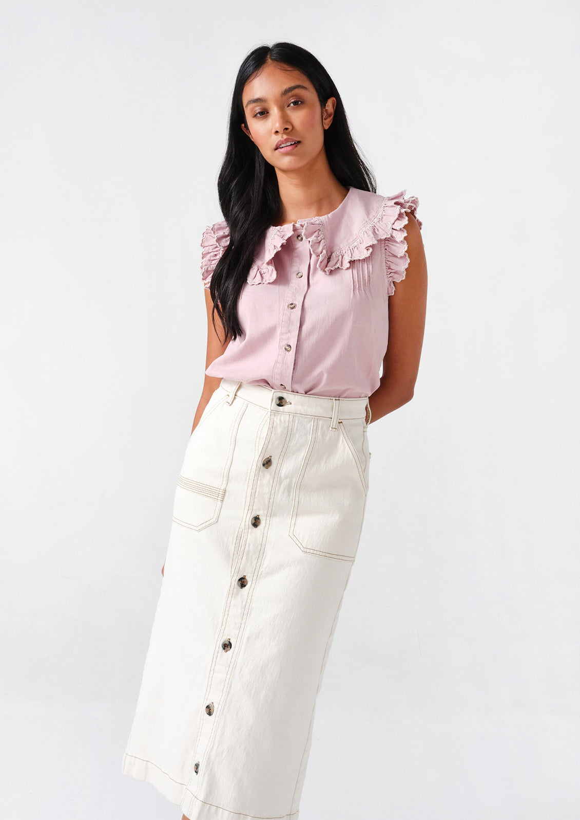 A woman in a white denim midi skirt and lilac top. 