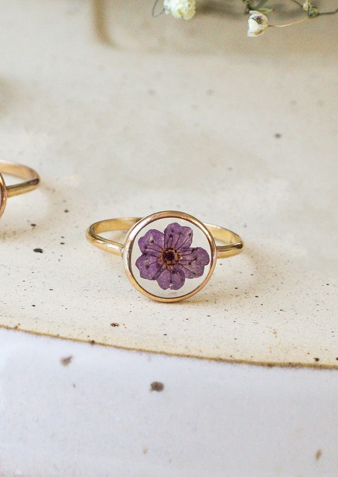 A gold round bezel ring showing purple flower on clear background.