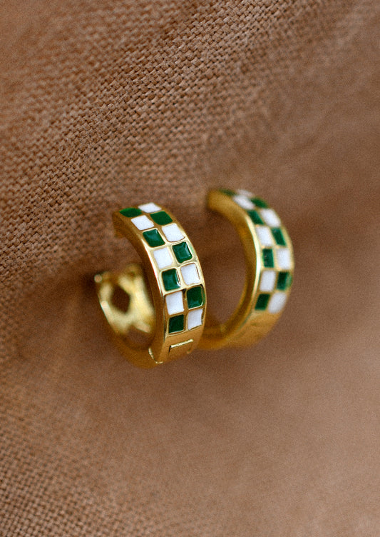 A pair of gold hoop earrings with green and white enamel checker pattern.