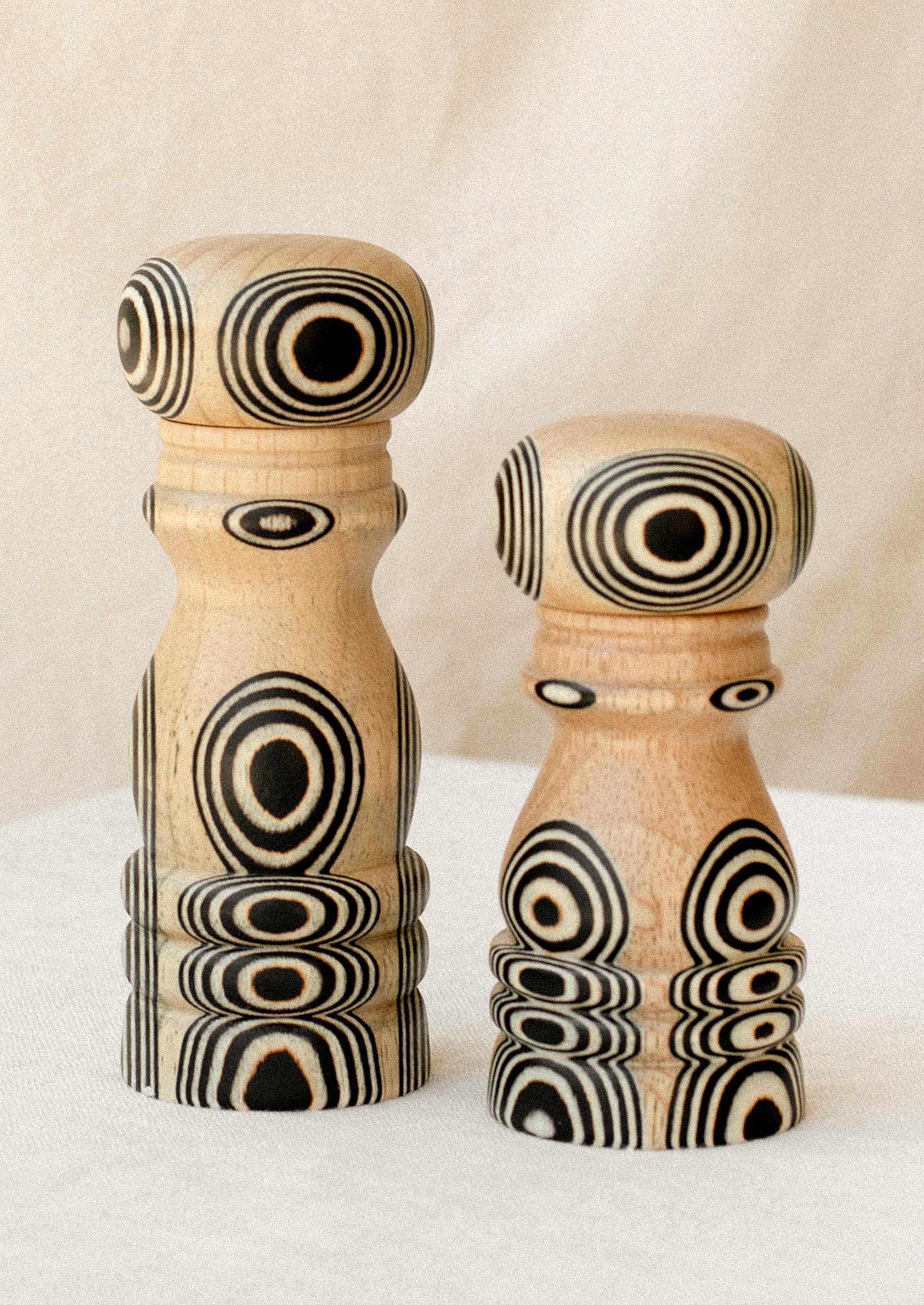 A short and tall pepper grinder in light wood with psychadelic black circle pattern.