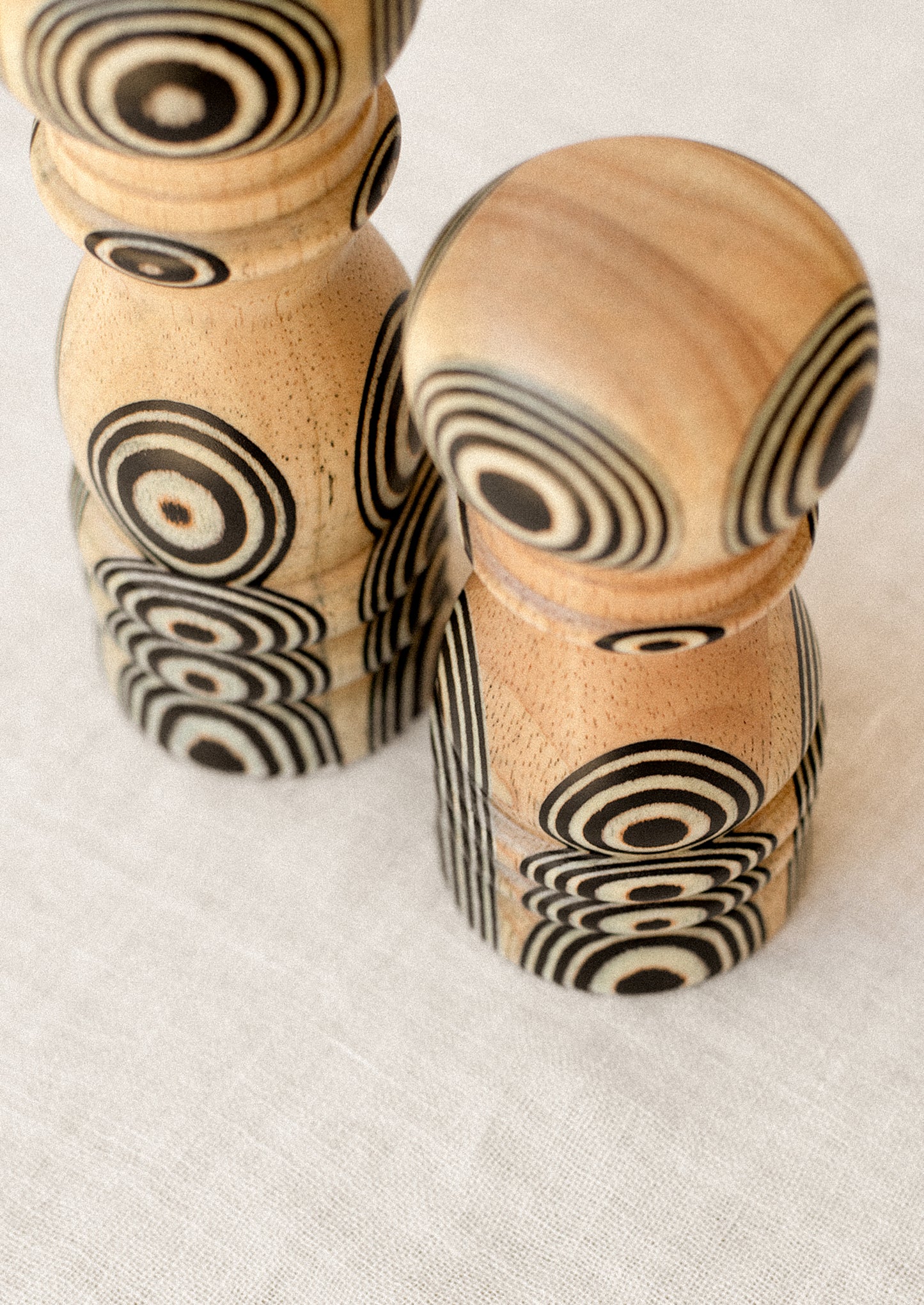 A short and tall pepper grinder in light wood with psychadelic black circle pattern.