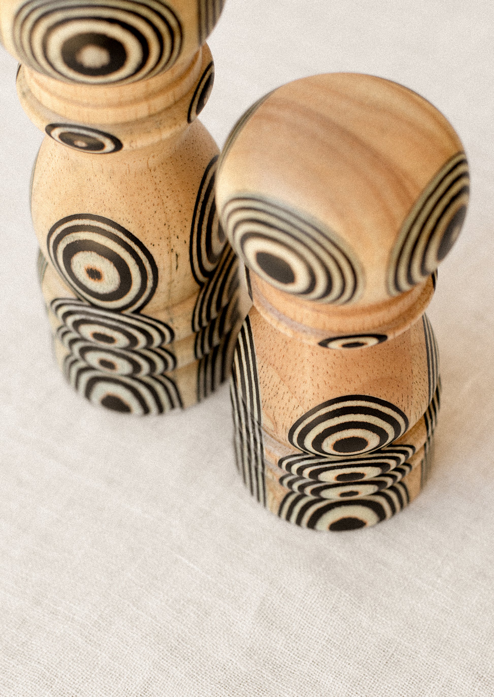 A short and tall pepper grinder in light wood with psychadelic black circle pattern.