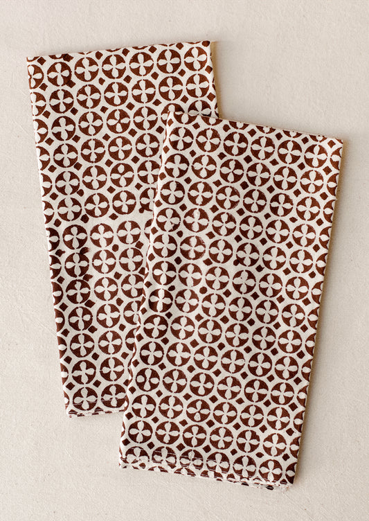 A pair of napkins with geometric circular cross pattern in brown and white.