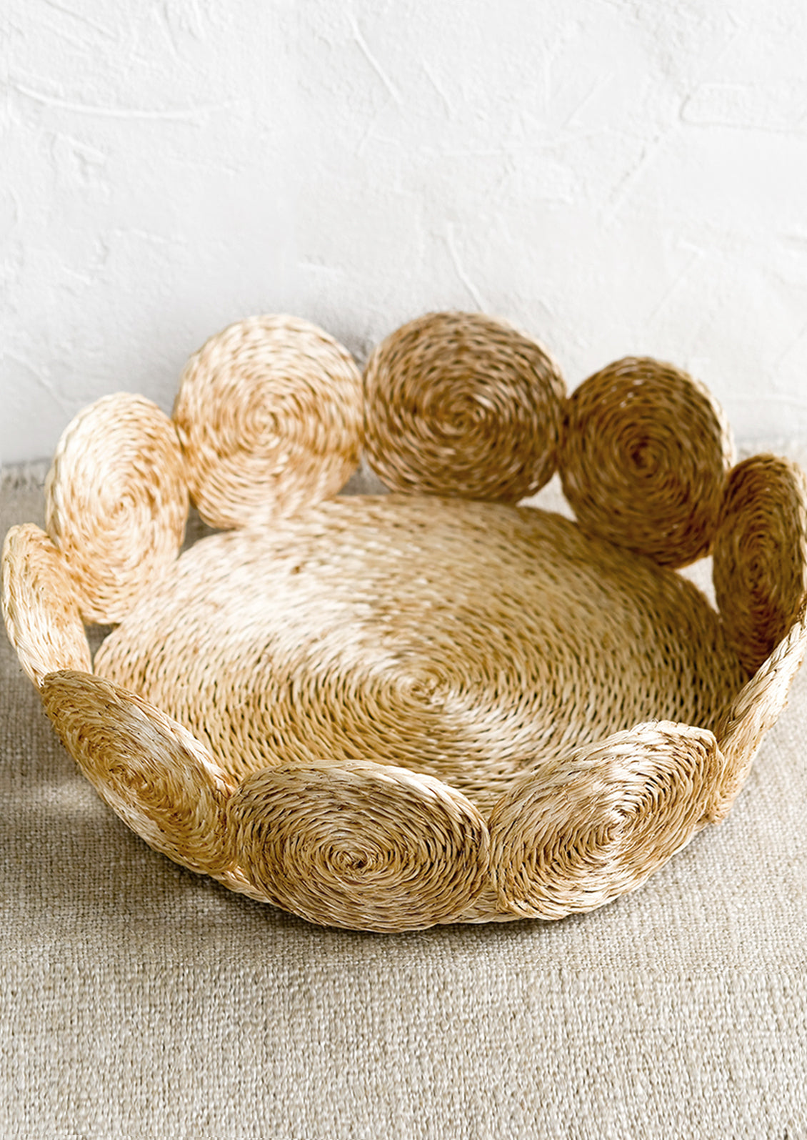 A round, shallow basket with woven circular border design in natural.