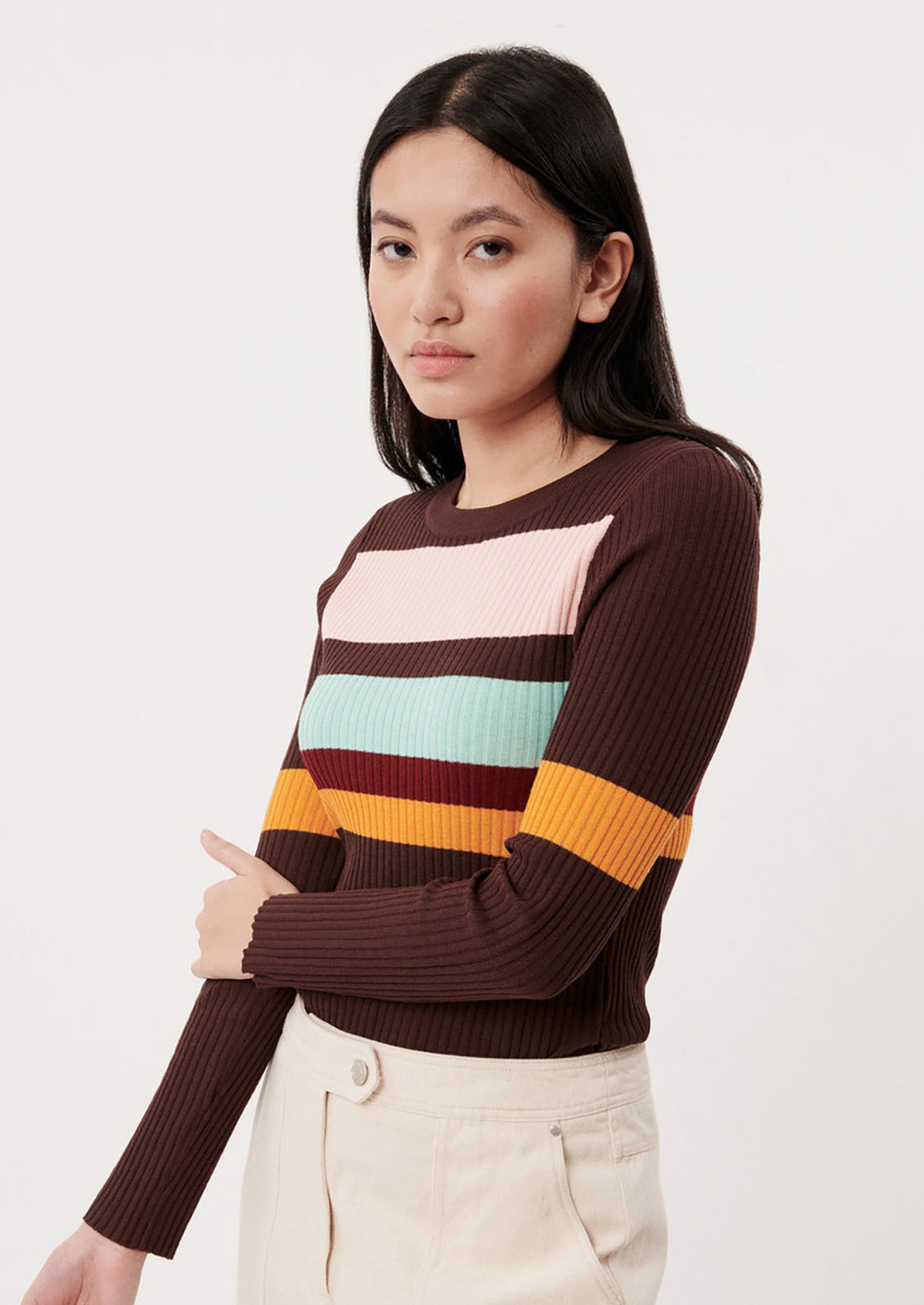 A woman wearing a brown form fitting sweater with multicolor stripes.