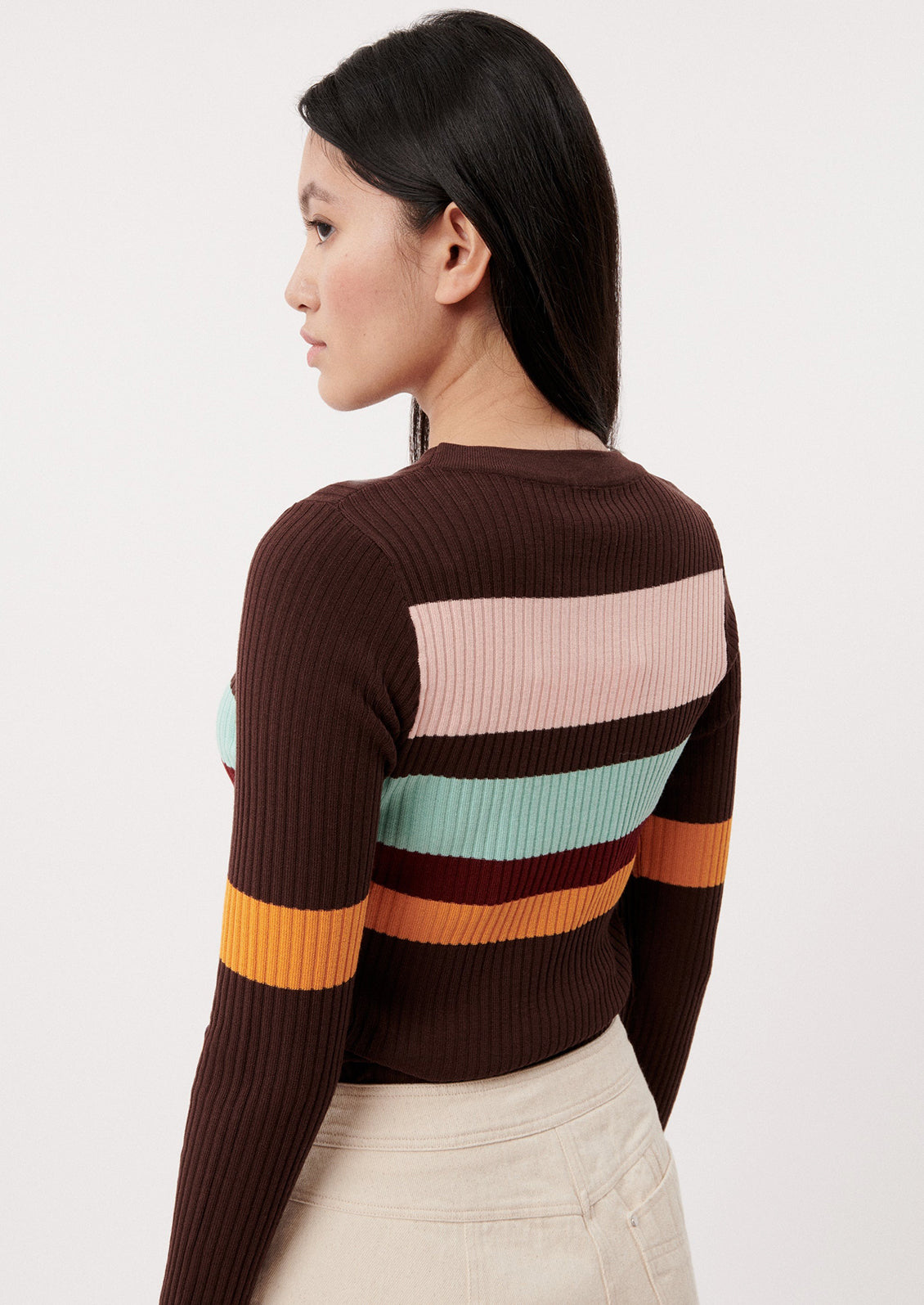 A woman wearing a brown form fitting sweater with multicolor stripes.