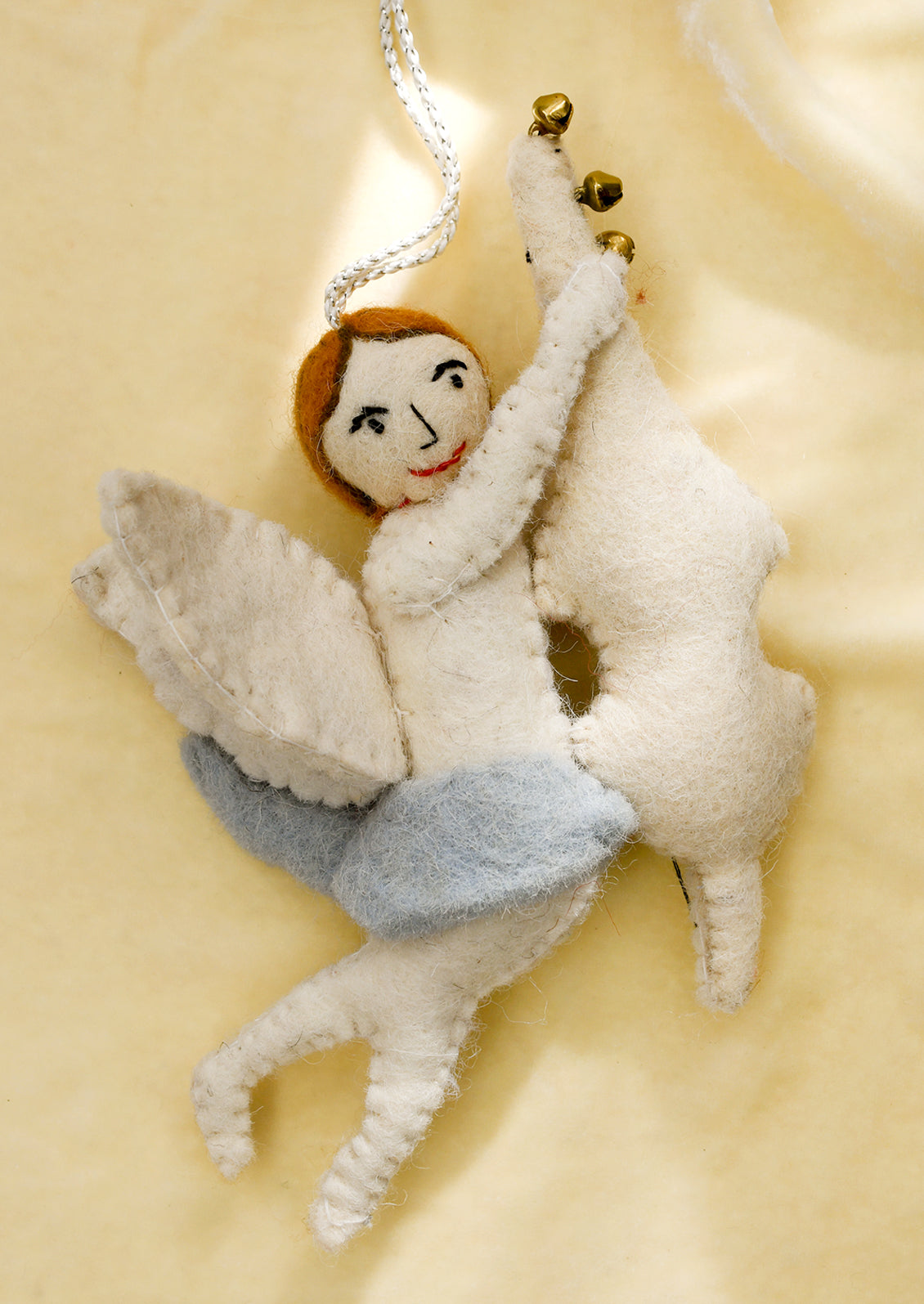 A felt ornament of a cherub wearing blue skirt, holding musical instrument.