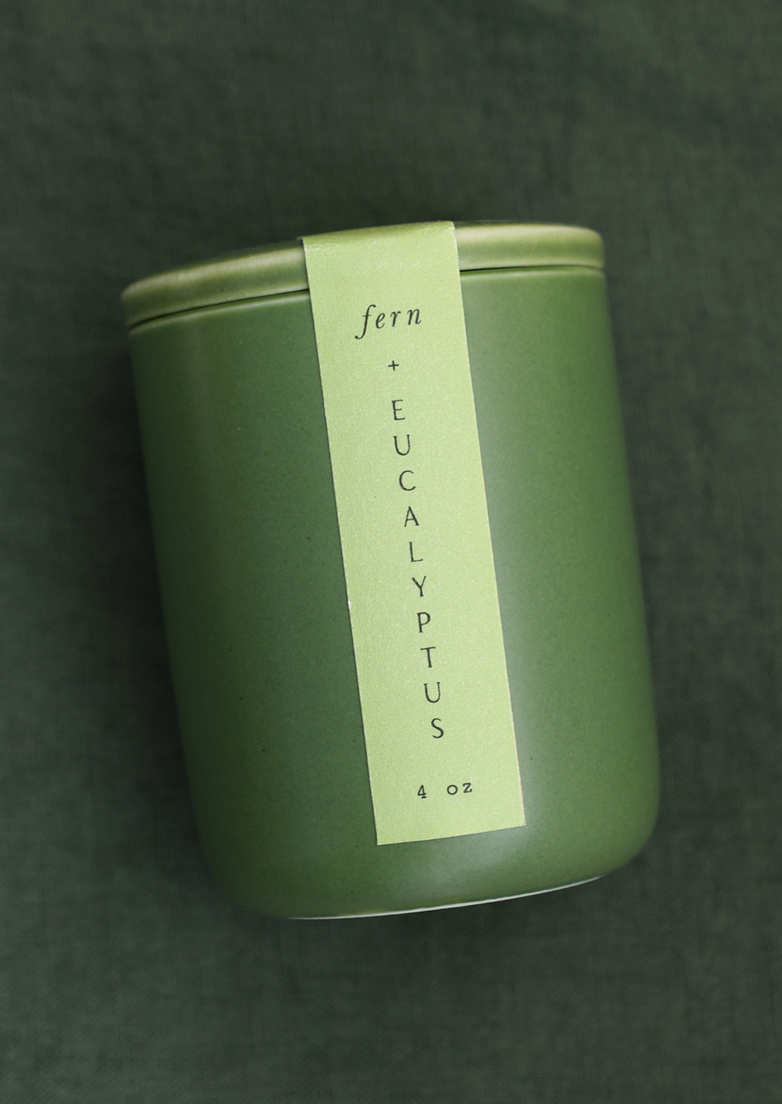 A small candle in lidded green ceramic jar in Fern & Eucalyptus scent.