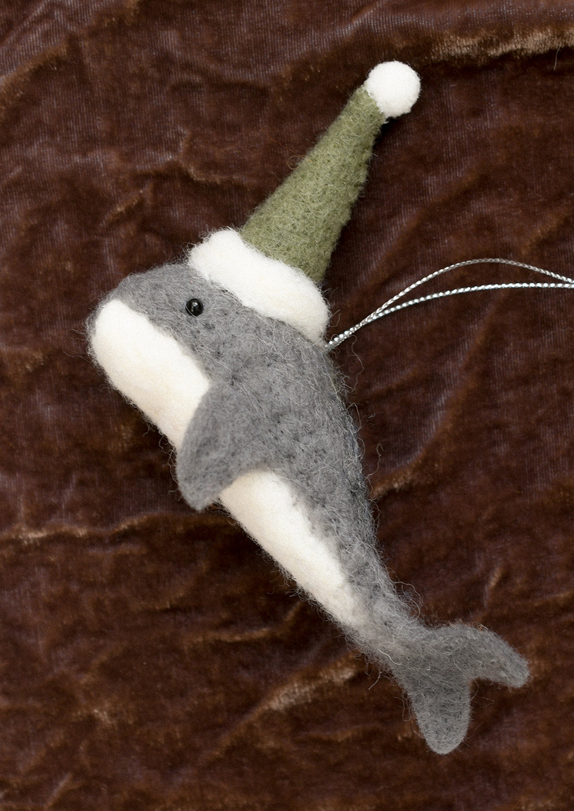 A felted wool ornament of whale in green party hat.