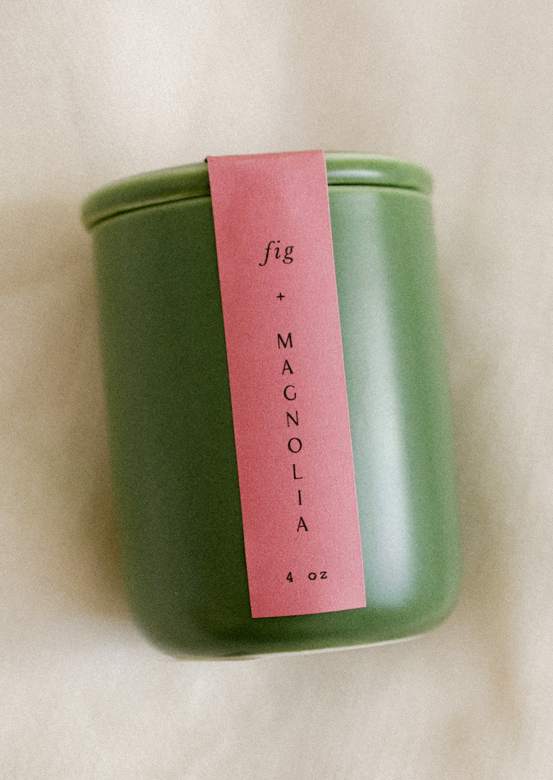 A small candle in lidded green ceramic jar in Fig & Magnolia scent.