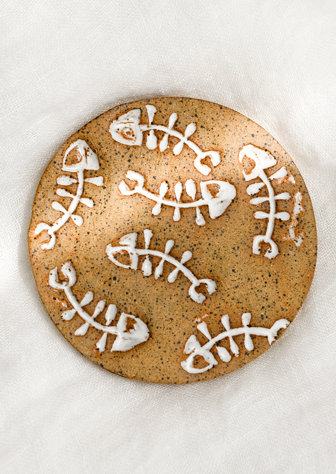 A round ceramic coaster in sand with white fishbone print.