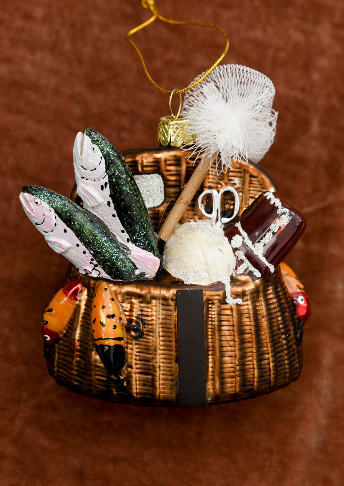 A glass ornament depicting a wicker basket holding fishing supplies.