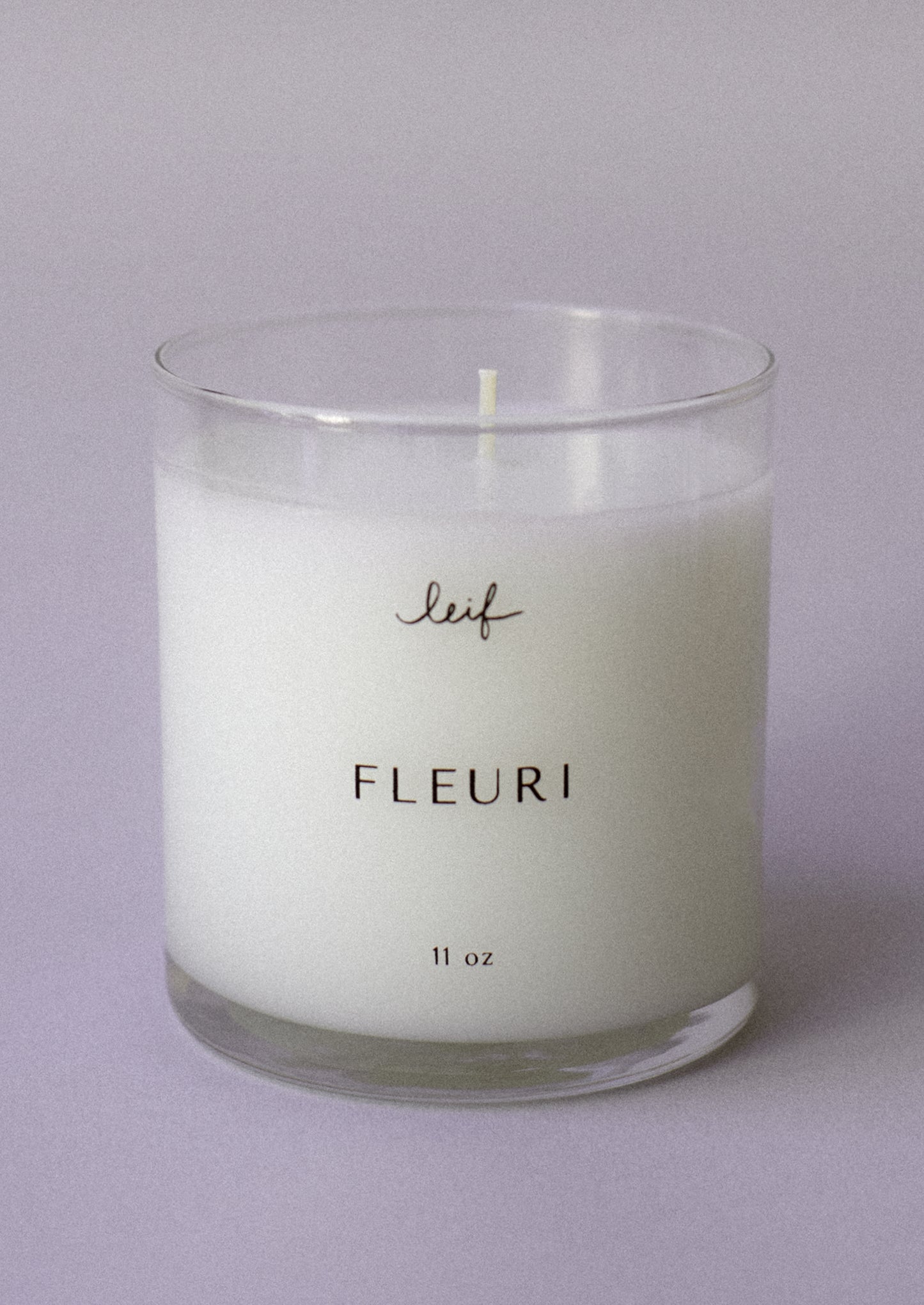 A candle in clear glass jar labeled "Fleuri".