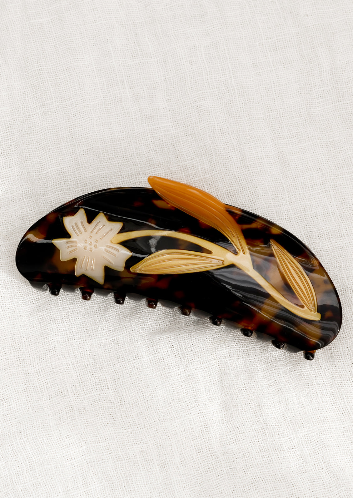 A dark brown tortoiseshell acetate hair claw with white flower.