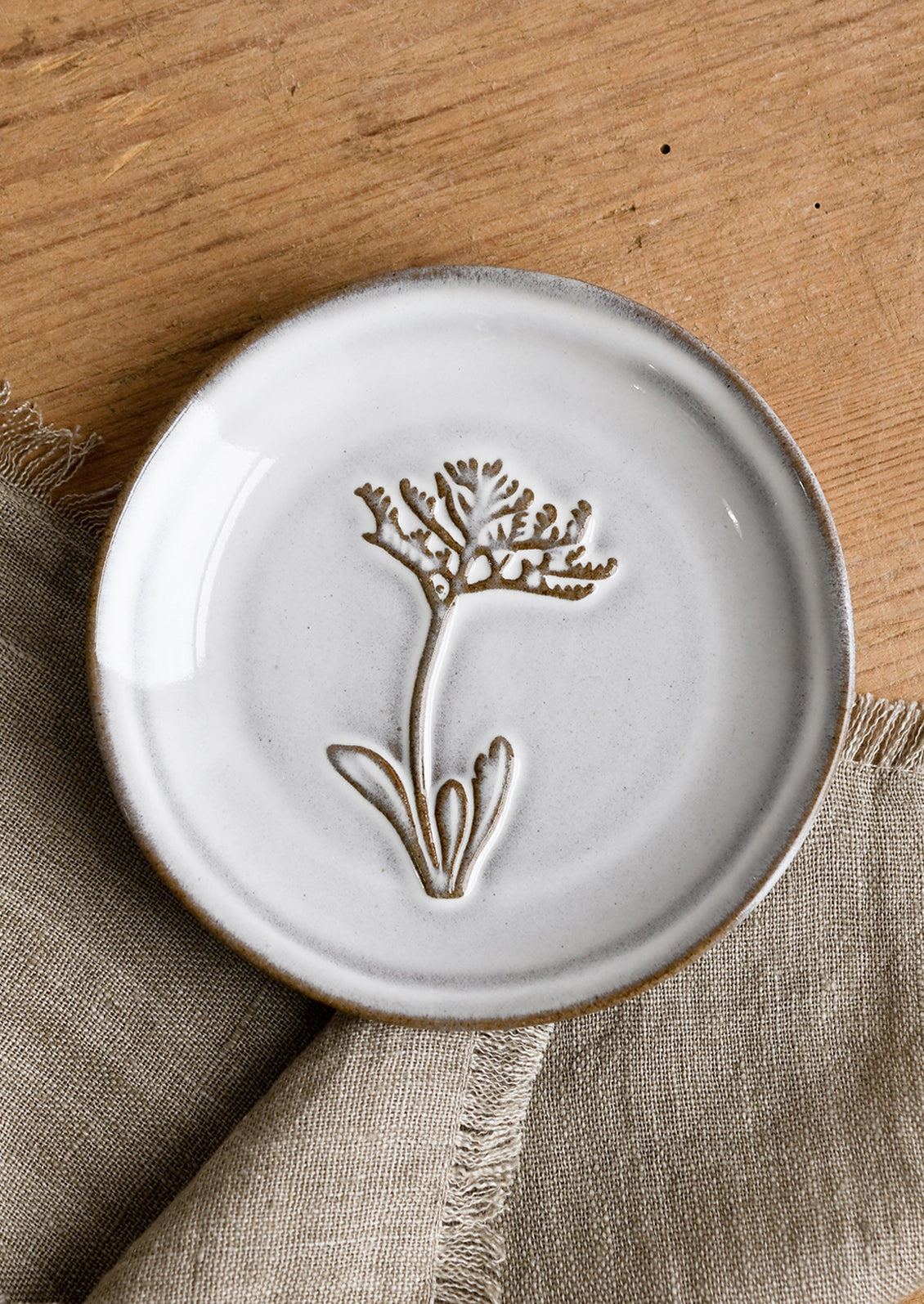 A grey glazed brown clay mini plate with raised flower design.