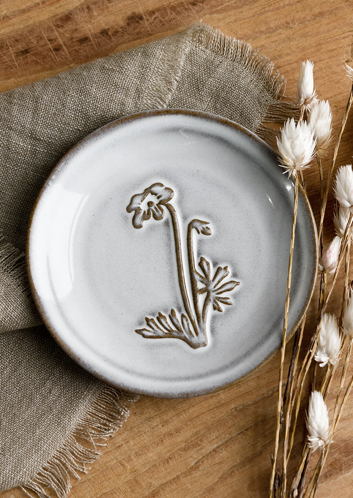 A grey glazed brown clay mini plate with raised flower design.