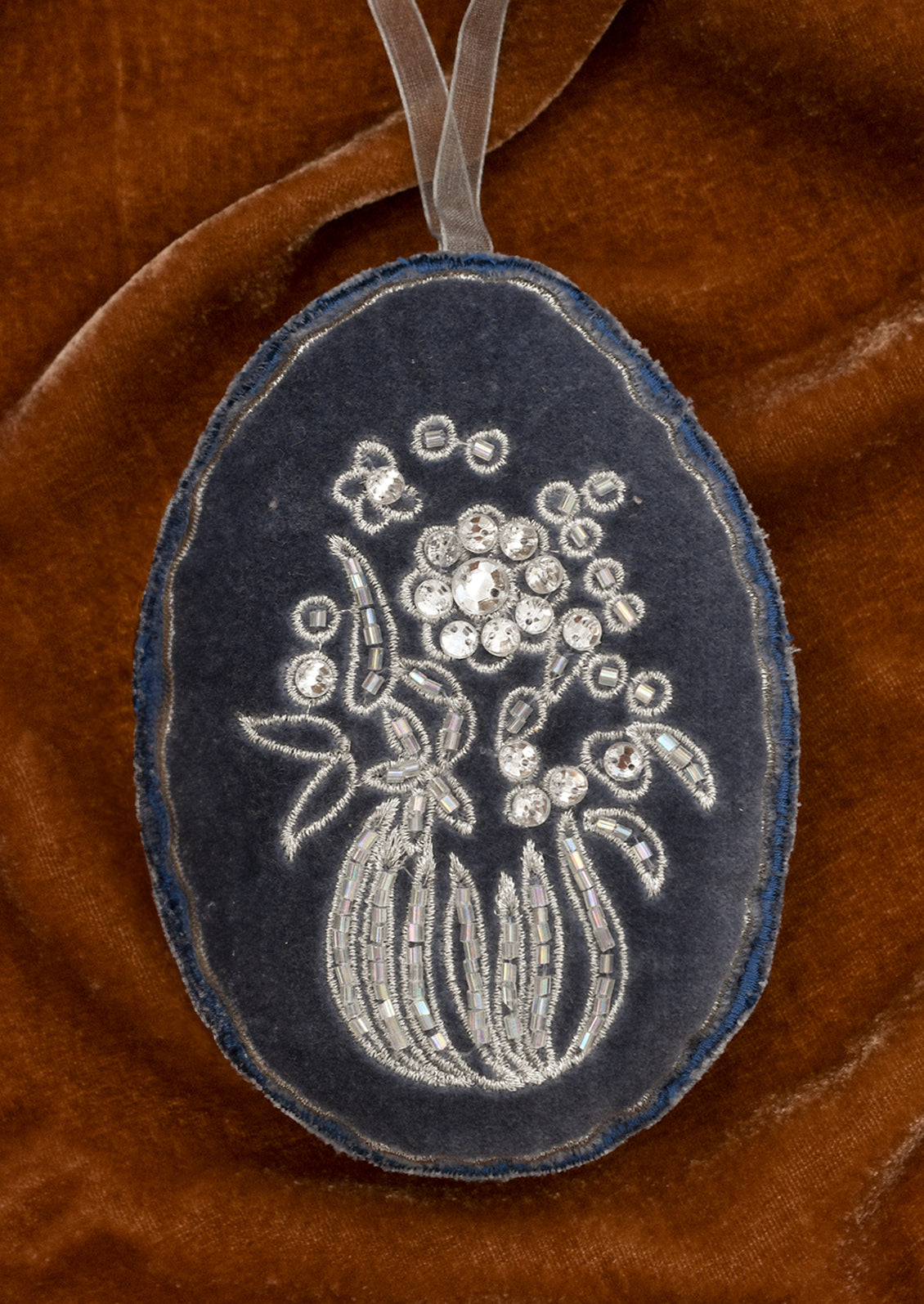 A blue velvet ornament with silver floral embroidery.