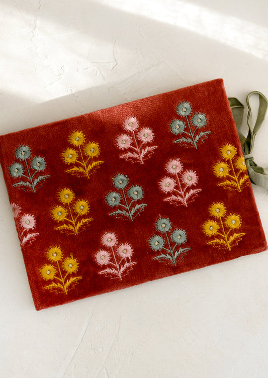 A rectangular journal in rust colored velvet with yellow, pink and mint floral embroidery.