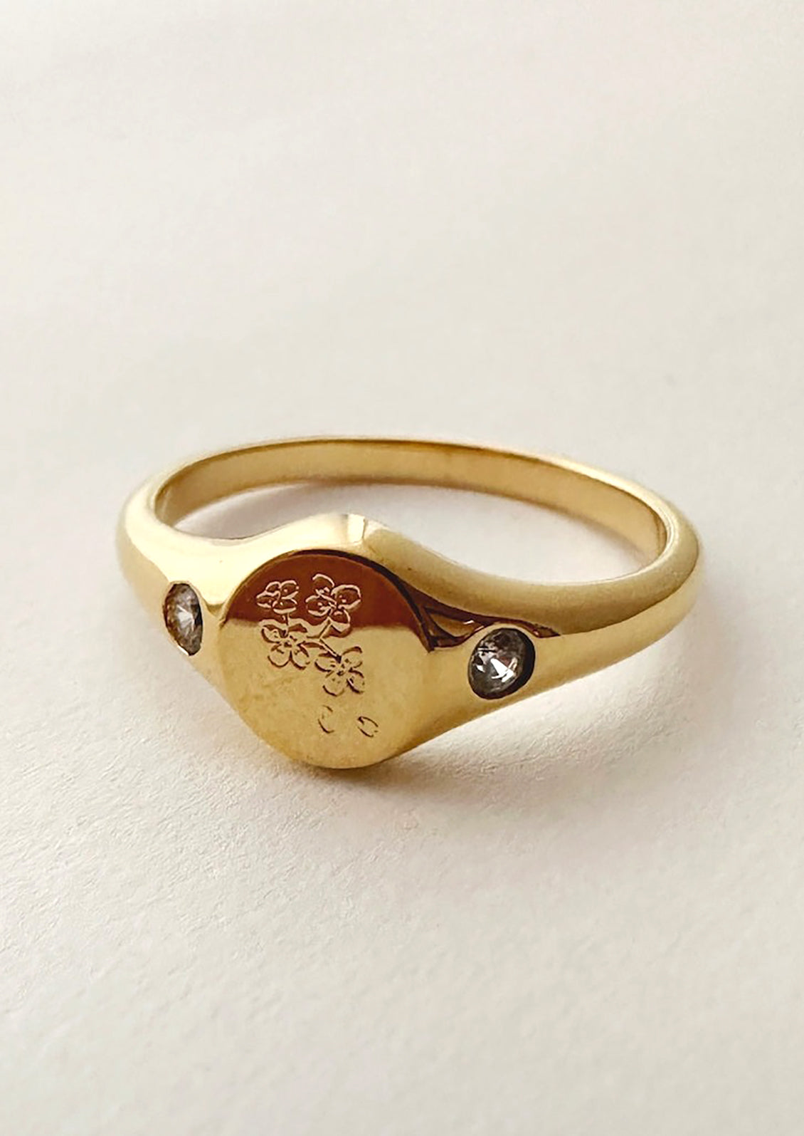 A gold signet ring with floral engraving with clear crystal on either side.