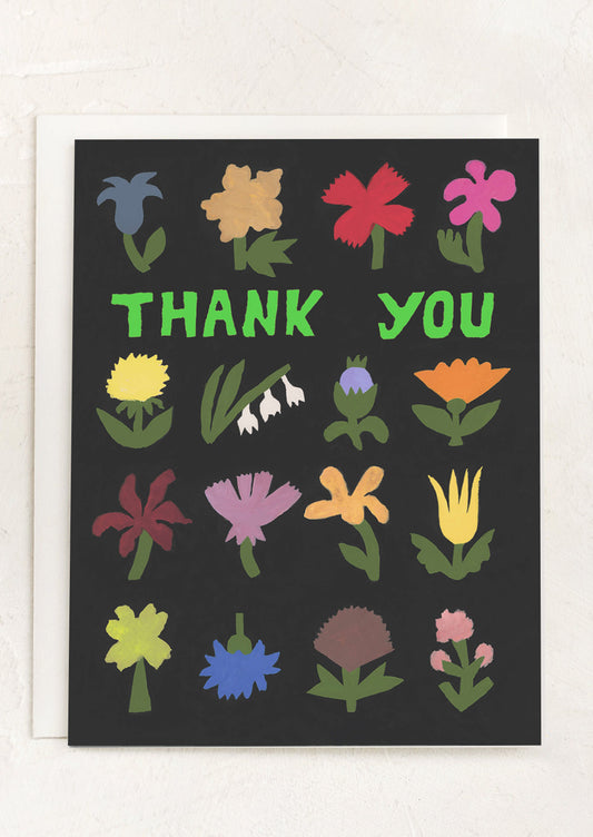 A black greeting card with multicolor flower print, neon green text reads "Thank You"