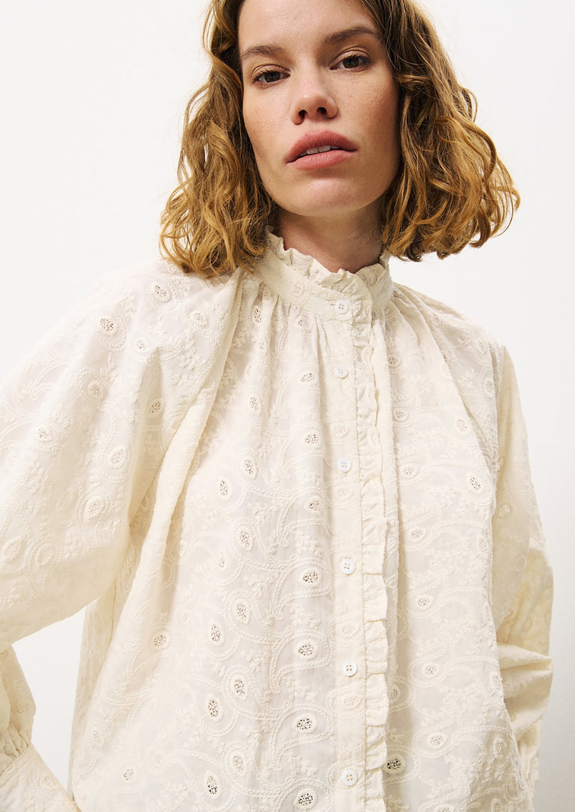 A woman wearing a cream cotton blouse with tonal paisley embroidery.