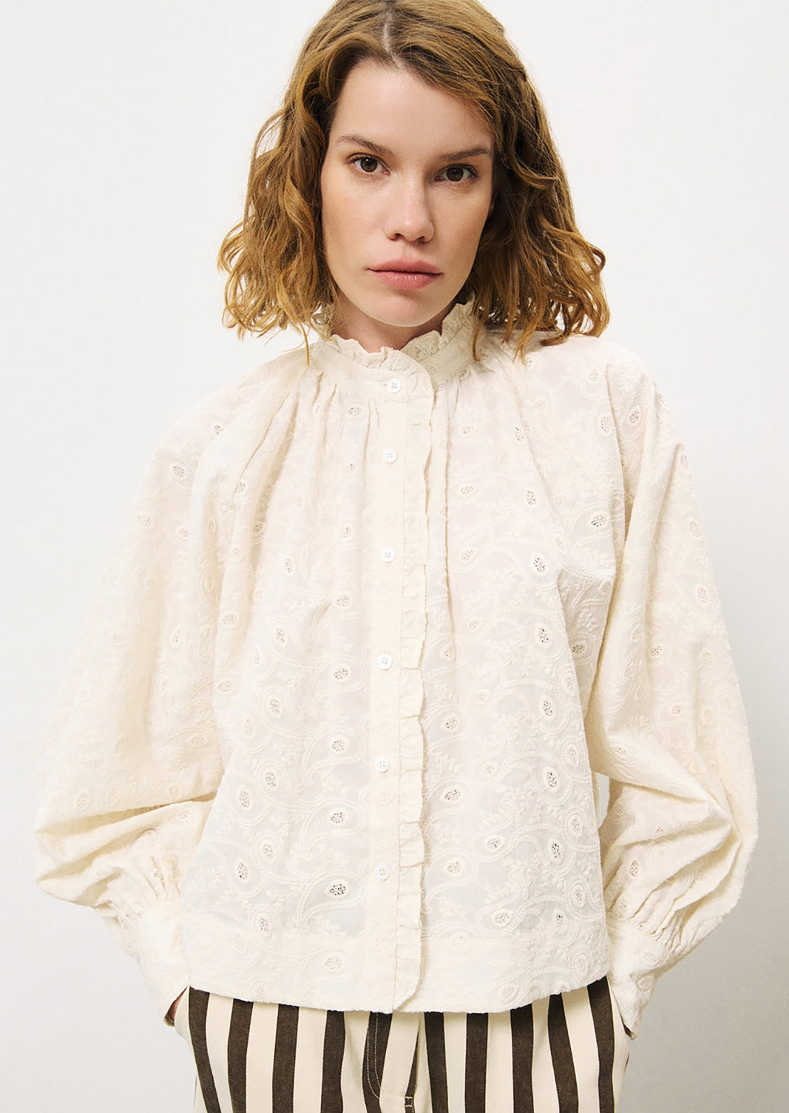 A woman wearing a cream cotton blouse with tonal paisley embroidery.