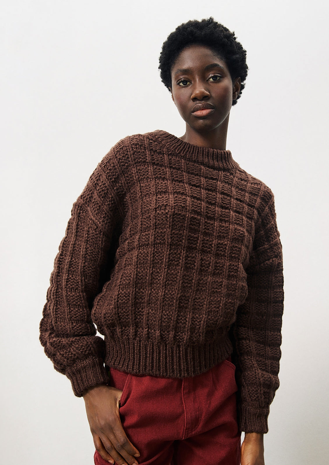 A person wearing a chunky waffle knit sweater in brown.