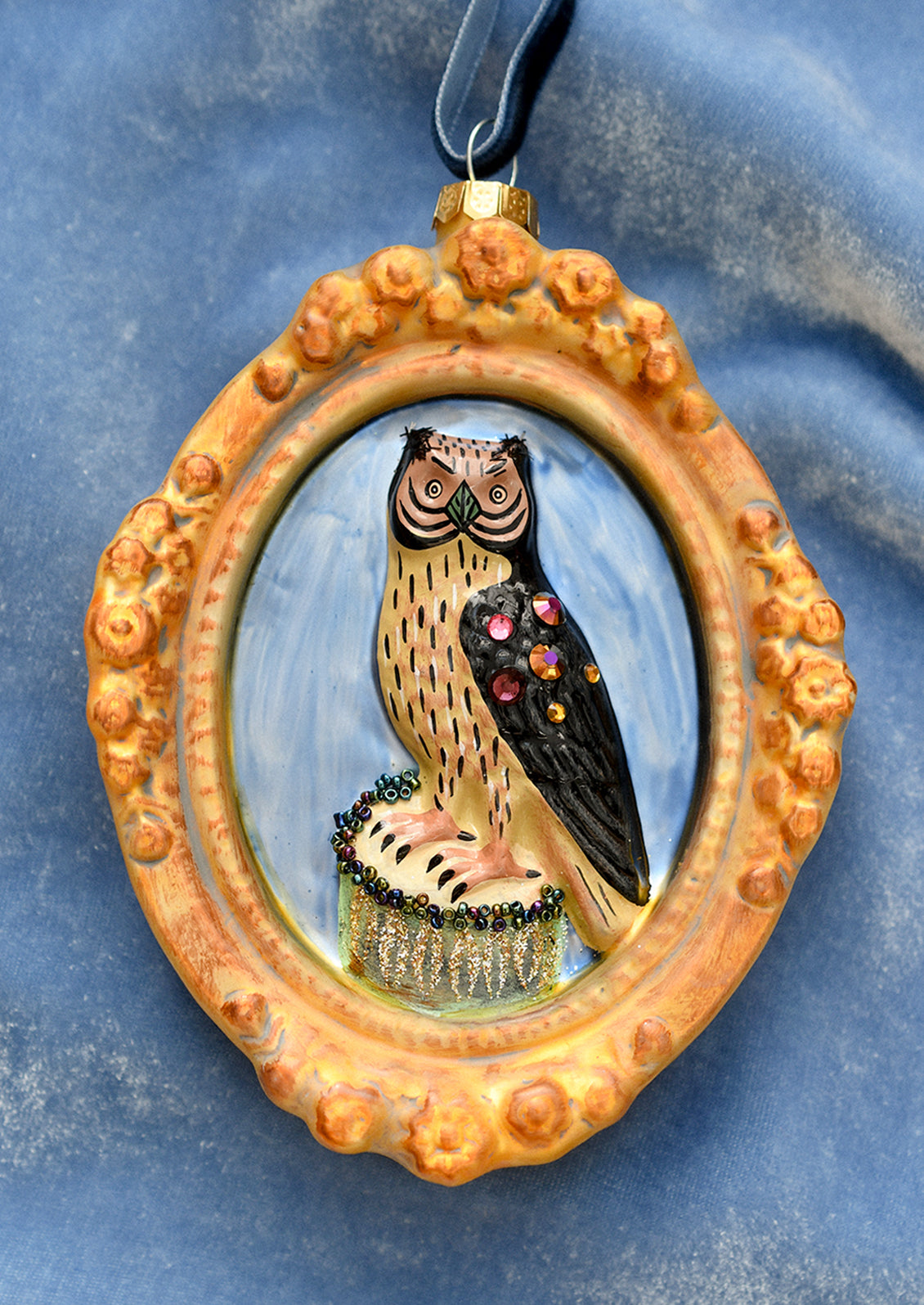 A glass ornament of a gilded oval frame around jewel detailed black owl.