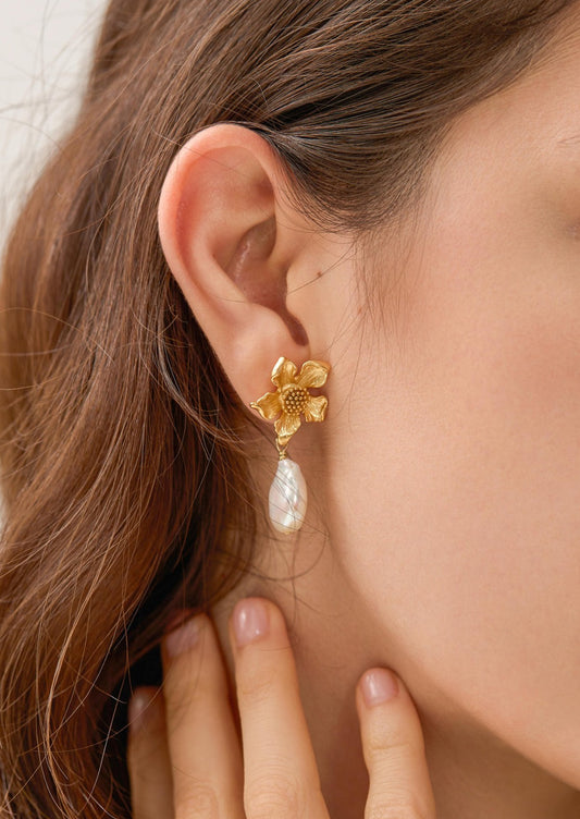 A pair of earrings with three dimensional gold flower post and dangling baroque pearl.