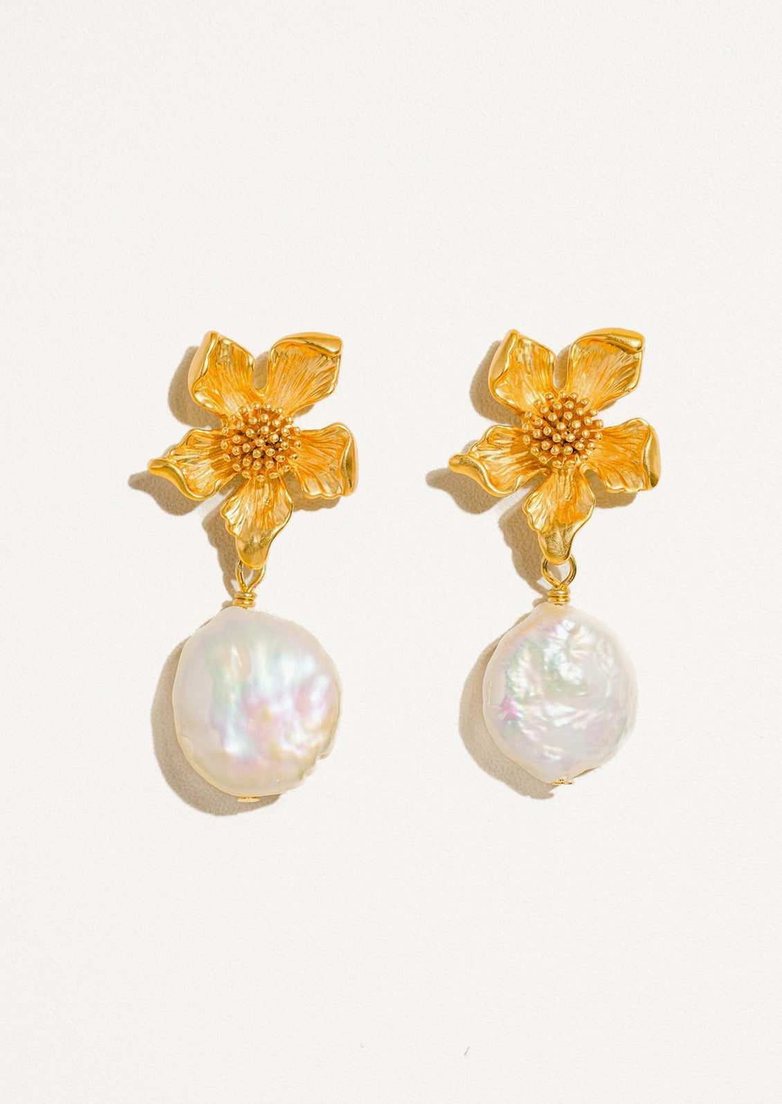 A pair of earrings with three dimensional gold flower post and dangling baroque pearl.