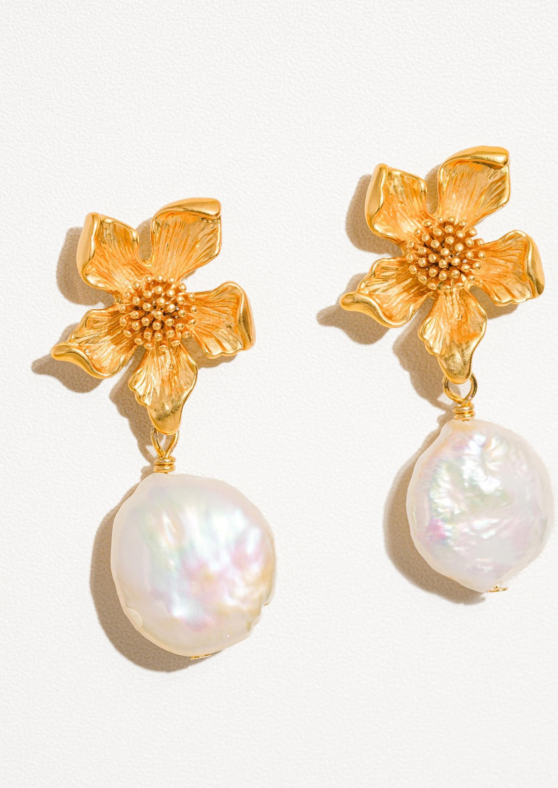 A pair of earrings with three dimensional gold flower post and dangling baroque pearl.