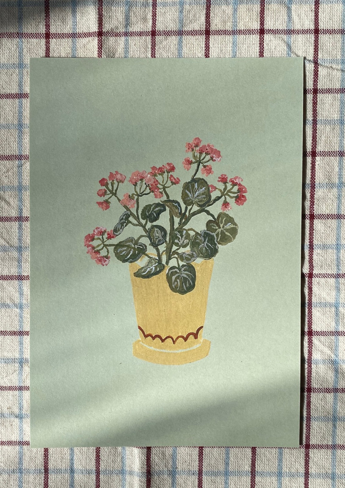 An illustrated art print of geraniums in yellow pot on mint green background.